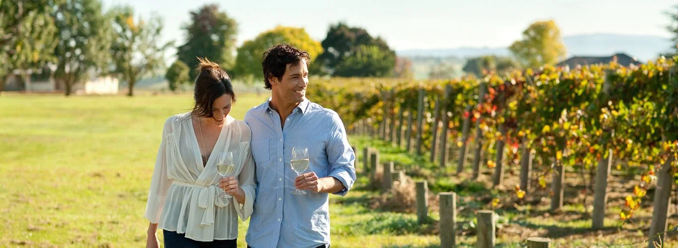 Couple walking beside vineyard rows with a glass of white wine